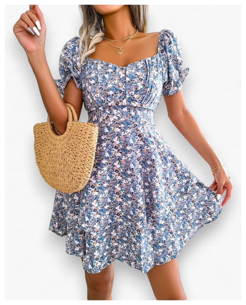 A woman displays a charming blue floral print dress from Eternal Gleams. The dress, featuring puffed short sleeves, a sweetheart neckline, and a fitted bodice with a flared skirt, offers a cool and calming style. The blue tone provides a serene and sophisticated look, making it perfect for any occasion. Paired with a gold necklace, the dress’s elegant and graceful nature shines through.